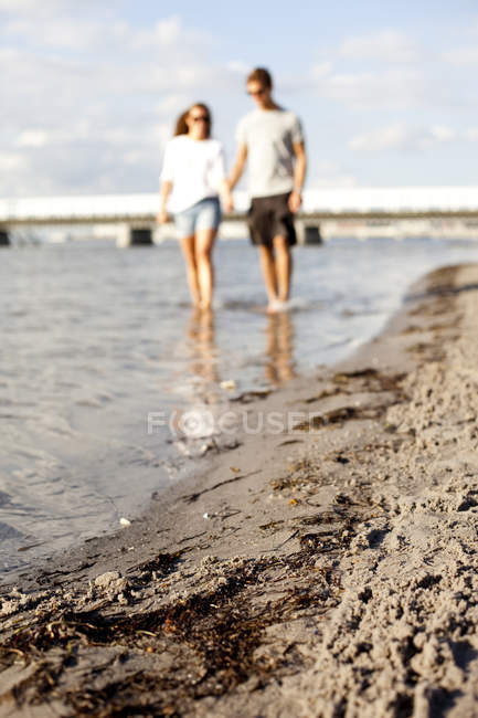 Couple tenant la main tout en marchant dans la mer — Photo de stock