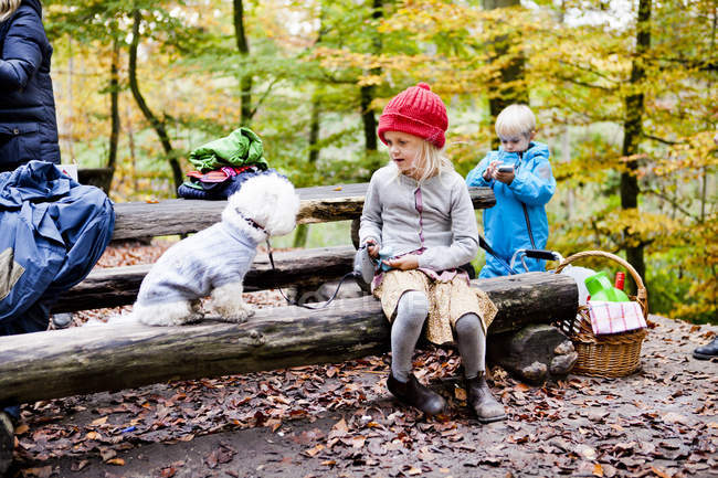 Girl sitting with Bichon Frise and brother on log — Stock Photo