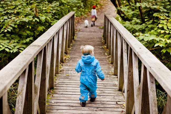 Boy walking on footbridge in forest — Stock Photo