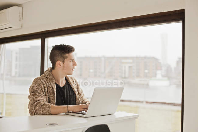 Человек с ноутбуком смотрит в окно — стоковое фото
