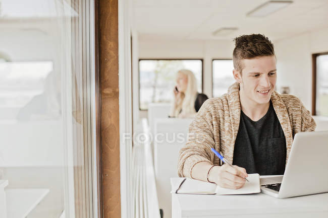 Человек пишет при использовании ноутбука — стоковое фото