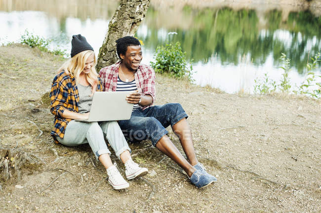 Пара с помощью ноутбука на берегу озера — стоковое фото