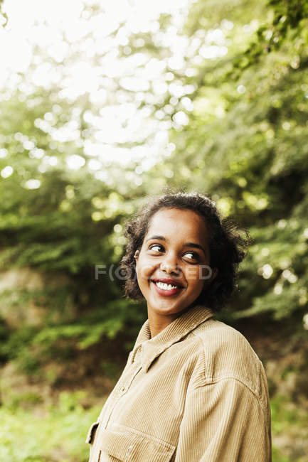 Femme souriant tout en regardant loin dans la forêt — Photo de stock