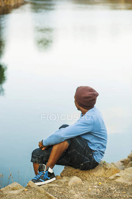 Человек, сидящий на скале у озера — стоковое фото