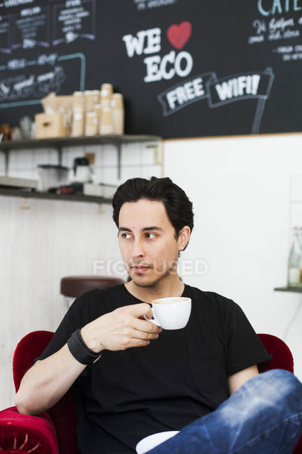 Мужчина отводит взгляд, держа чашку кофе — стоковое фото