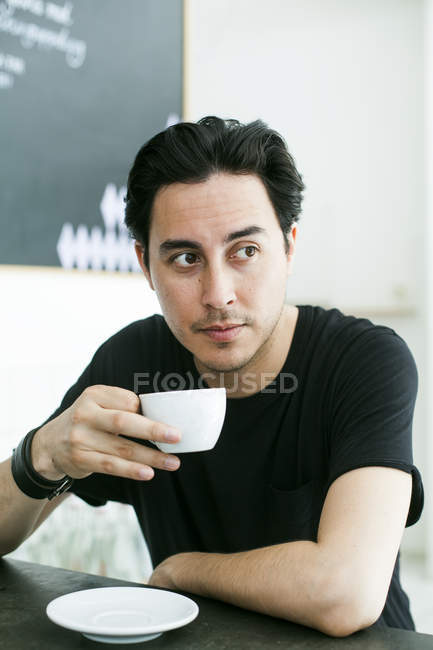 Мужчина держит чашку кофе, сидя за столом — стоковое фото
