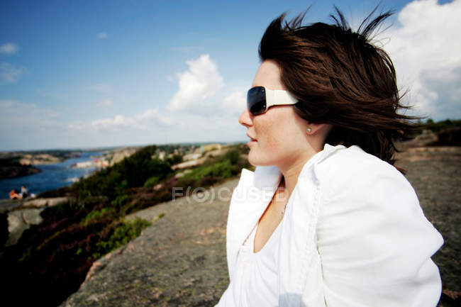 Side view of woman wearing sunglasses while relaxing on rocky coastline — Stock Photo