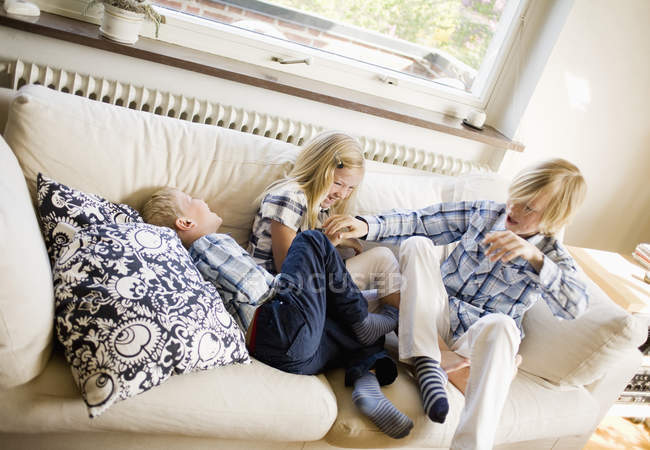 Vista de ángulo alto de tres hermanos jugando en el sofá en casa - foto de stock