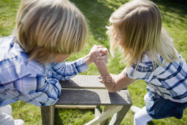 High angle view of siblings arm wrestling on wooden table in back yard — Stock Photo
