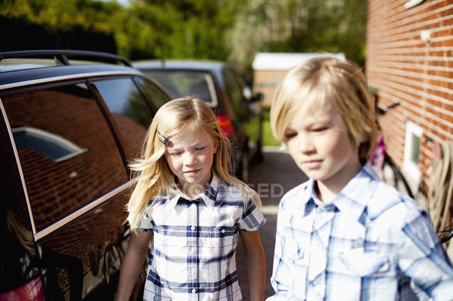 Brother and sister standing by car in back yard — Stock Photo