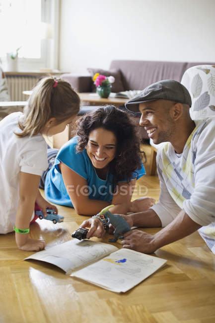 Family enjoying with toys and book on hardwood floor — Stock Photo