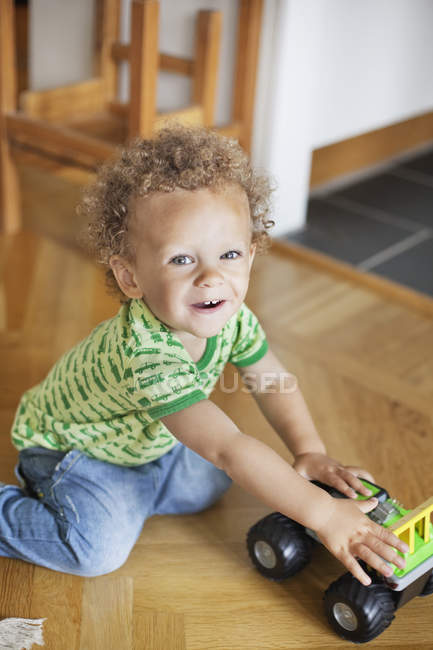 Garçon jouer avec jouet voiture sur plancher de bois franc — Photo de stock