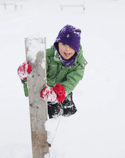 Menino ajoelhado por poste de madeira na neve — Fotografia de Stock