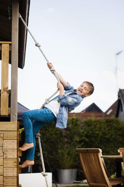 Boy climbing on rope in back yard — Stock Photo