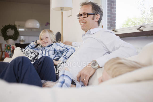 Зрелый мужчина сидит с сыновьями на диване дома — стоковое фото