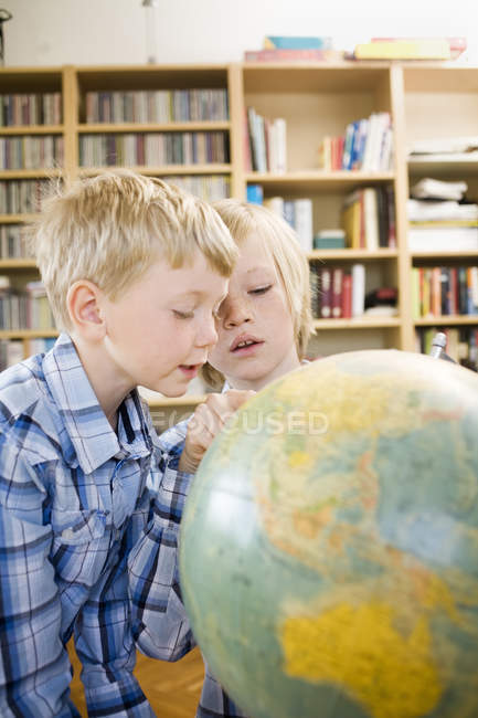 Мальчики смотрят вместе на глобус в интерьере дома — стоковое фото