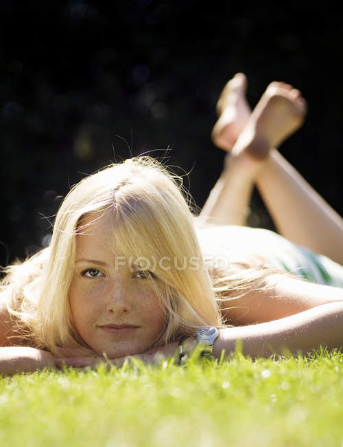 Mujer rubia tumbada sobre hierba verde y mirando en la cámara - foto de stock
