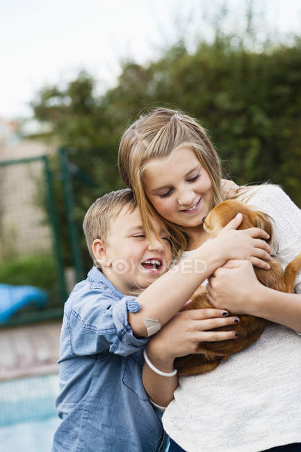Щасливі брати і сестри, що обіймають собаку — стокове фото