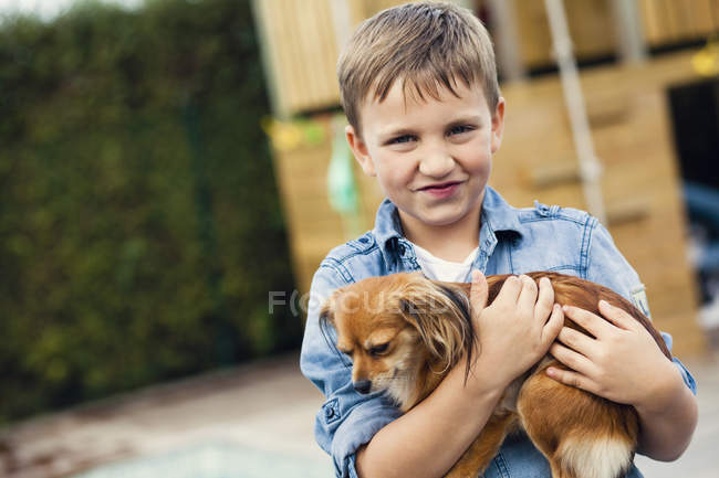 Счастливый мальчик, обнимающий Чихуахуа — стоковое фото
