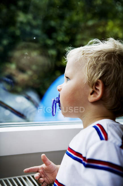 Side view of boy with pacifier while looking in window — Stock Photo
