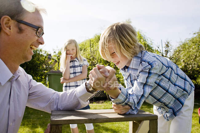 Girl looking at father arm wrestling with brother at back yard — Stock Photo