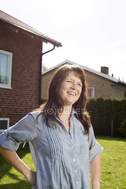 Femme souriante debout dans la cour arrière et regardant loin — Photo de stock
