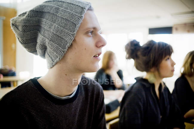 Чоловік студент дивиться далеко, сидячи з однокласниками в класі — стокове фото