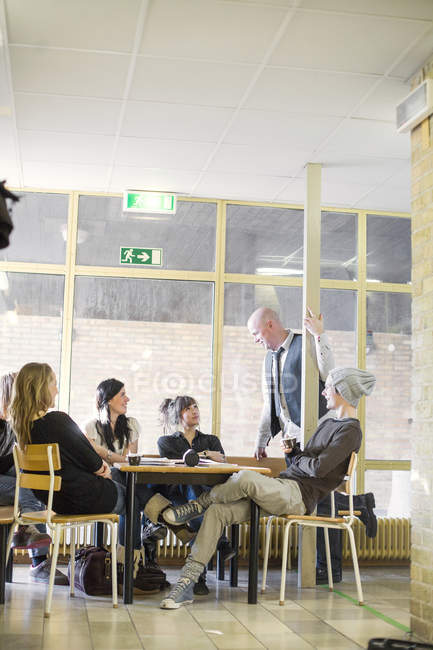 Insegnante che parla con gli studenti delle scuole superiori seduti nella sala comune — Foto stock
