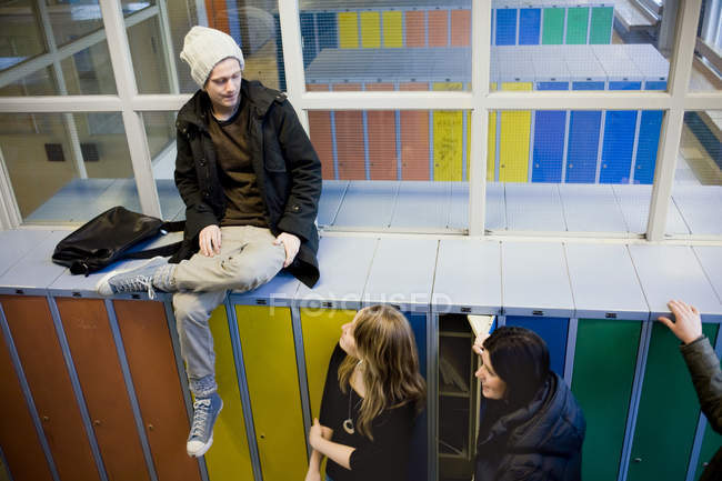 Hochwinkelaufnahme eines Mannes, der auf Schließfächern sitzt, während er Freundinnen in der Universität ansieht — Stockfoto