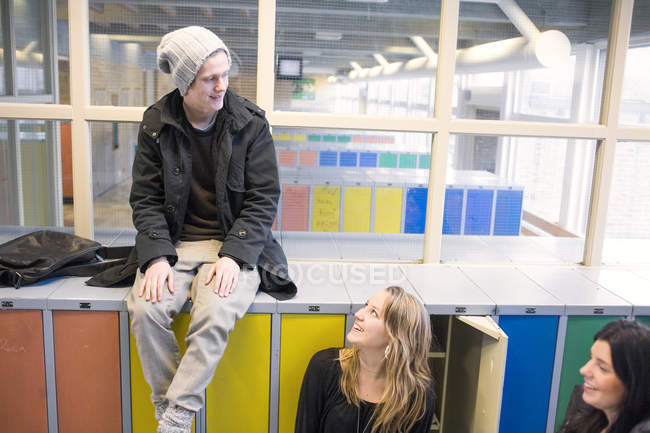 Gymnasiast sitzt auf Schließfächern und spricht mit Klassenkameradinnen — Stockfoto