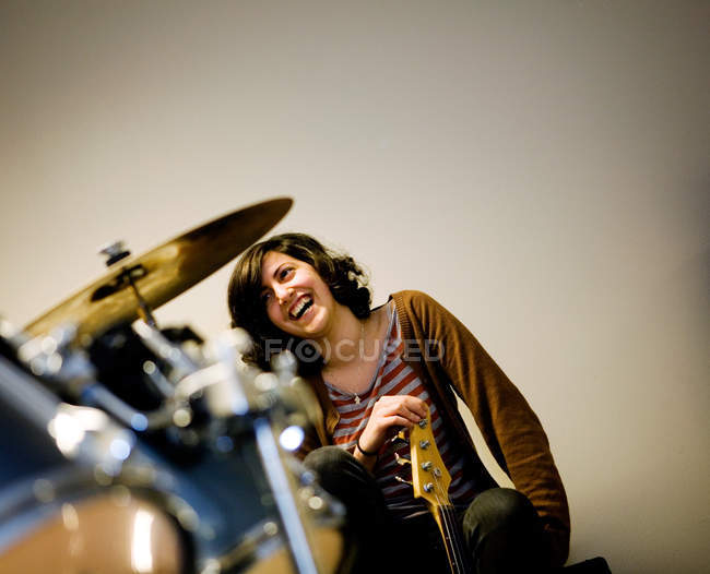 Laughing woman holding bass guitar near drum in studio room — Stock Photo
