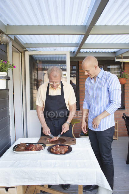Man looking at father cutting meat — Stock Photo
