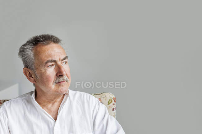 Uomo anziano seduto contro il muro grigio — Foto stock