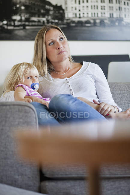 Madre e hija sentadas en un sofá - foto de stock