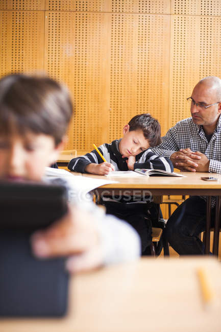 Teacher assisting schoolboy at desk — Stock Photo