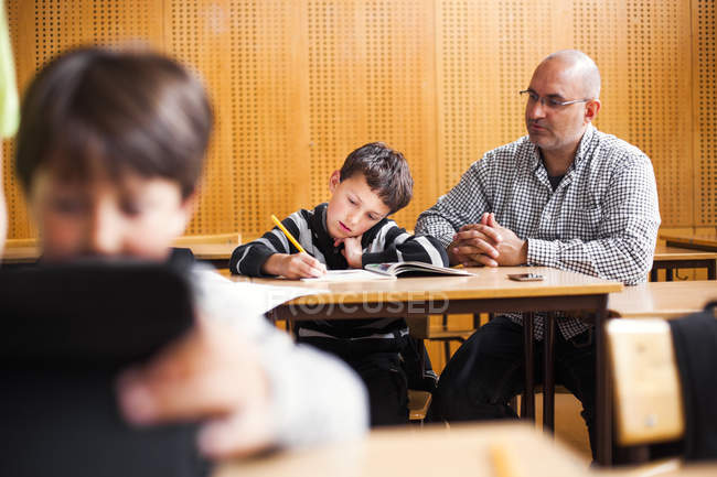Teacher assisting schoolboy studying — Stock Photo