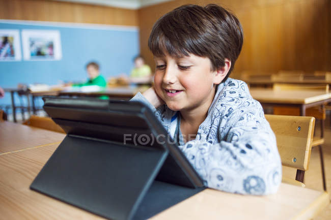 Écolier souriant utilisant une tablette numérique — Photo de stock