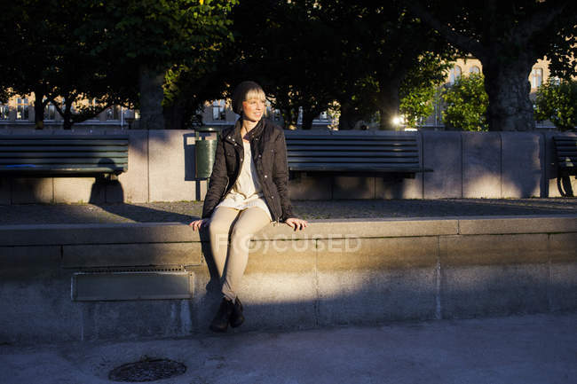 Женщина, сидящая на удерживающей стене в парке — стоковое фото