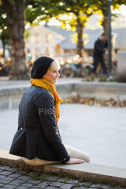 Frau sitzt auf Stützmauer im Park — Stockfoto
