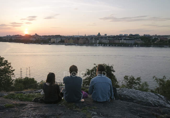 Persone sedute vicino al fiume al tramonto — Foto stock