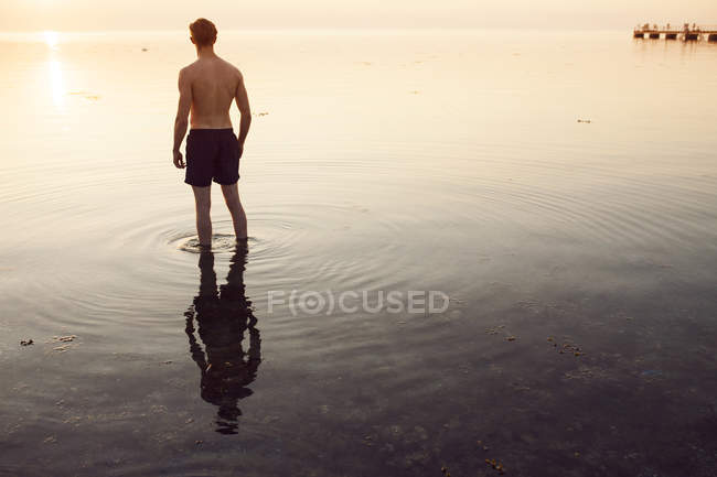 Человек в шортах бродит в море на закате — стоковое фото