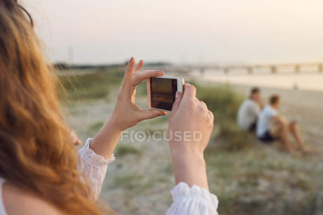 Mujer joven tomando fotos en la playa - foto de stock