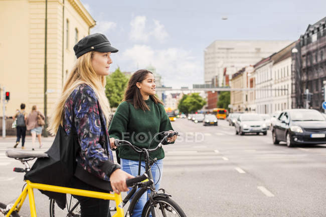 Mujeres jóvenes empujando bicicletas en la ciudad - foto de stock