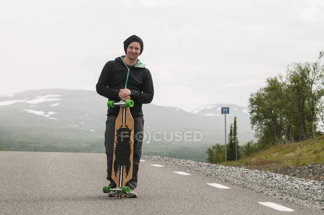 Человек со скейтбордом, стоящий на дороге — стоковое фото