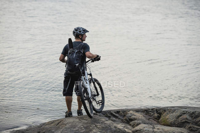 Man with bicycle standing by lake — Stock Photo