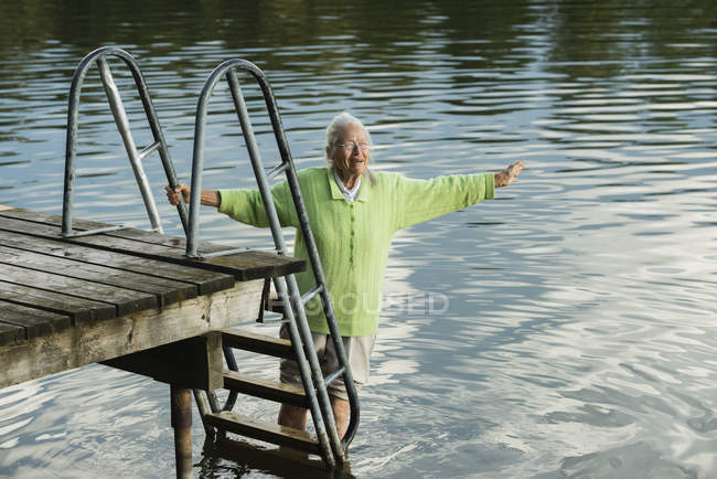 Mujer por muelle, vadeando en el agua - foto de stock