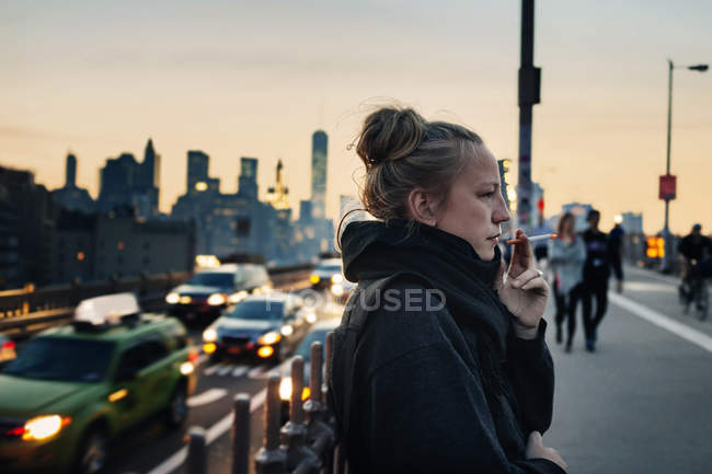 Woman standing on bridge and smoking cigarette — Stock Photo
