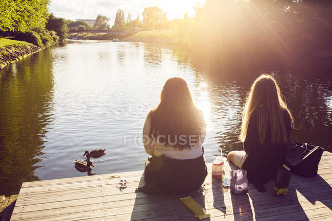 Молодые женщины сидят на пирсе — стоковое фото