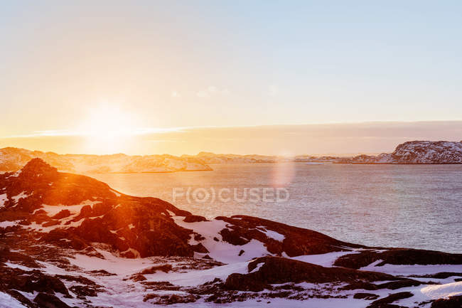 Snowy coastline by ocean at sunset — Stock Photo