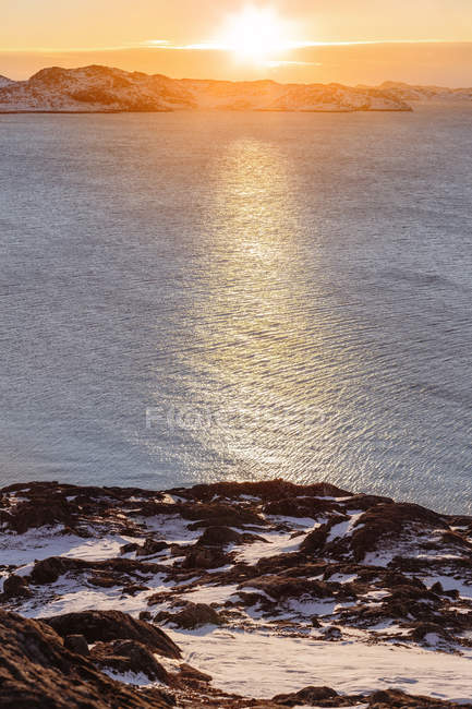 Snowy coastline by ocean at sunset — Stock Photo